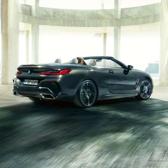 BMW M850i xDrive Cabrio, πίσω λήψη τριών τετάρτων. BMW M850i xDrive Cabrio σε γκρι Dravit μεταλλικό με ανοικτή υφασμάτινη οροφή, πίσω λήψη τριών τετάρτων, διερχόμενη μέσα από τσιμεντένιο κτίριο.