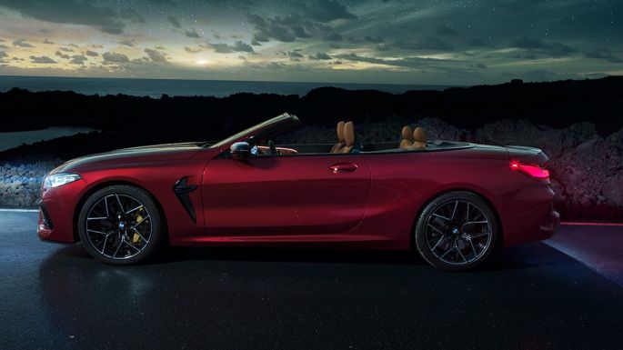 BMW M8 Competition Cabrio, πλαϊνή λήψη. BMW Μ8 Competition Cabrio σε κόκκινο Motegi μεταλλικό με ανοικτή υφασμάτινη οροφή, πλαϊνή λήψη, σταθμευμένη, νύχτα κάτω από έναστρο ουρανό.