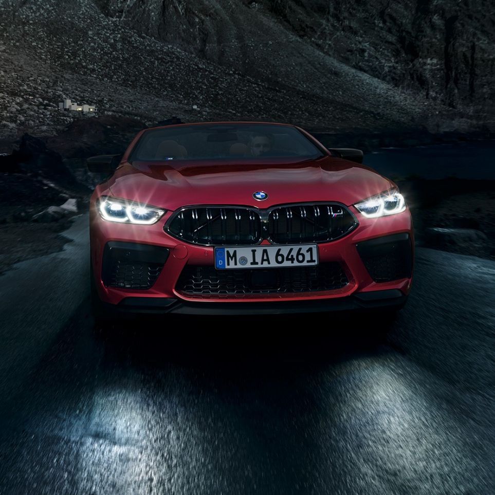 BMW M8 Competition Cabrio, μπροστινή λήψη. BMW Μ8 Competition Cabrio σε κόκκινο Motegi μεταλλικό με αναμμένους προβολείς, μπροστινή λήψη, κινούμενη τη νύχτα.