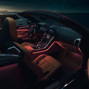 BMW M8 Competition Cabrio, εσωτερικό. BMW M8 Competition Cabrio με ανοικτή υφασμάτινη οροφή, εσωτερικό με κόκκινο ατμοσφαιρικό φωτισμό τη νύχτα.