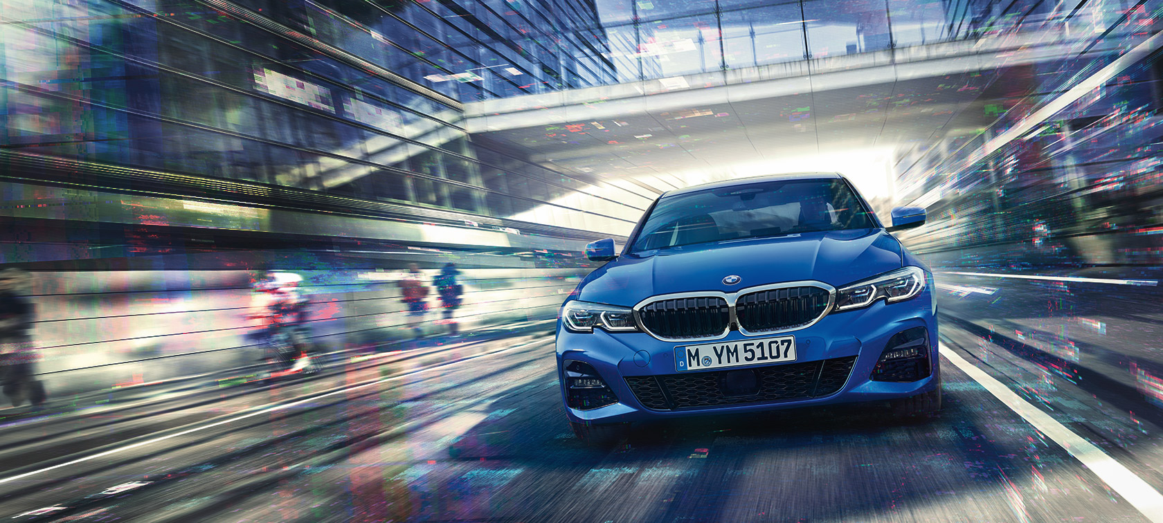 Μπροστινή λήψη της BMW Σειράς 3 Sedan (G20) σε κίνηση, την ημέρα, κάτω από γυάλινο κτίριο.
