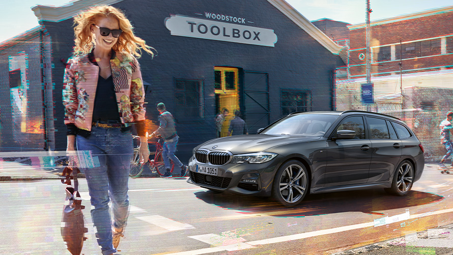 BMW Σειρά 3 Touring (G21), μπροστινή λήψη τριών τετάρτων με γυναίκα μπροστά από κατάστημα ξυλουργικών εργαλείων Γυναίκα διασχίζει τον δρόμο μπροστά από μία BMW Σειρά 3 Touring (G21), μπροστά από ένα κατάστημα ξυλουργικών εργαλείων