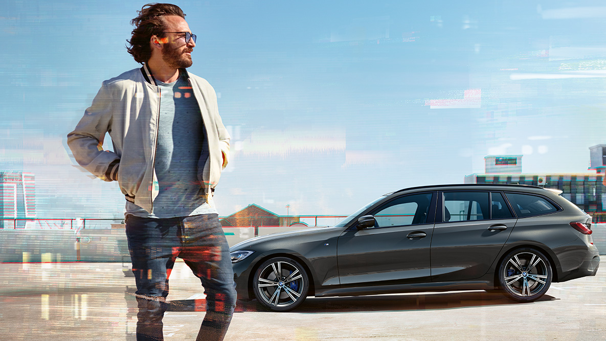 BMW Σειρά 3 Touring (G21), μπροστινή λήψη τριών τετάρτων, σχεδίαση BMW Σειρά 3 Touring (G21), γκρι Dravite, μπροστινή λήψη τριών τετάρτων σε κίνηση, σε γέφυρα, μπροστά από αγροτικό σκηνικό
