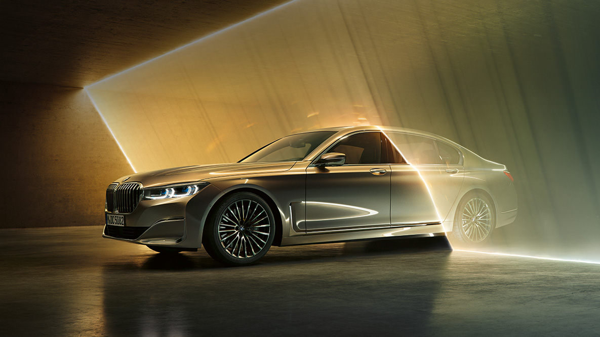 BMW Σειρά 7 Sedan σε μπροστινή όψη τριών τετάρτων BMW Σειρά 7 Sedan: γκρι BMW σε μπροστινή όψη τριών τετάρτων, πλαισιωμένη από φωτεινές ακτίνες