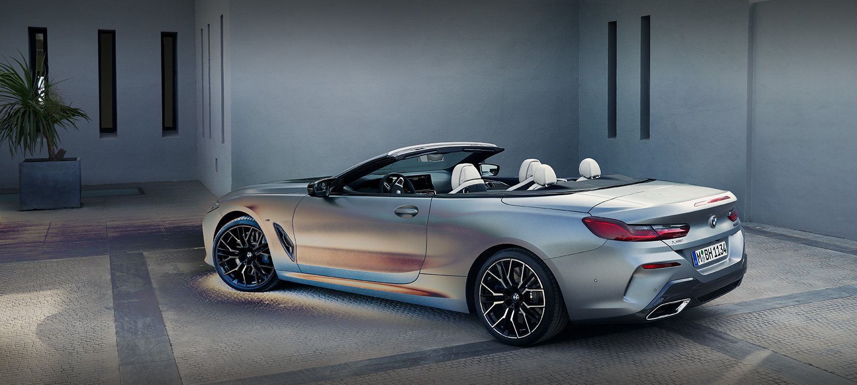 Άντρας στηρίζεται στην η νέα BMW Σειρά 8 Cabrio, G14, LCI Facelift, 2022, BMW Individual γκρι Frozen Pure μη μεταλλικό, πλαϊνή λήψη τριών τετάρτων, σταθμευμένη μπροστά από κτίριο με αντρικό μοντέλο