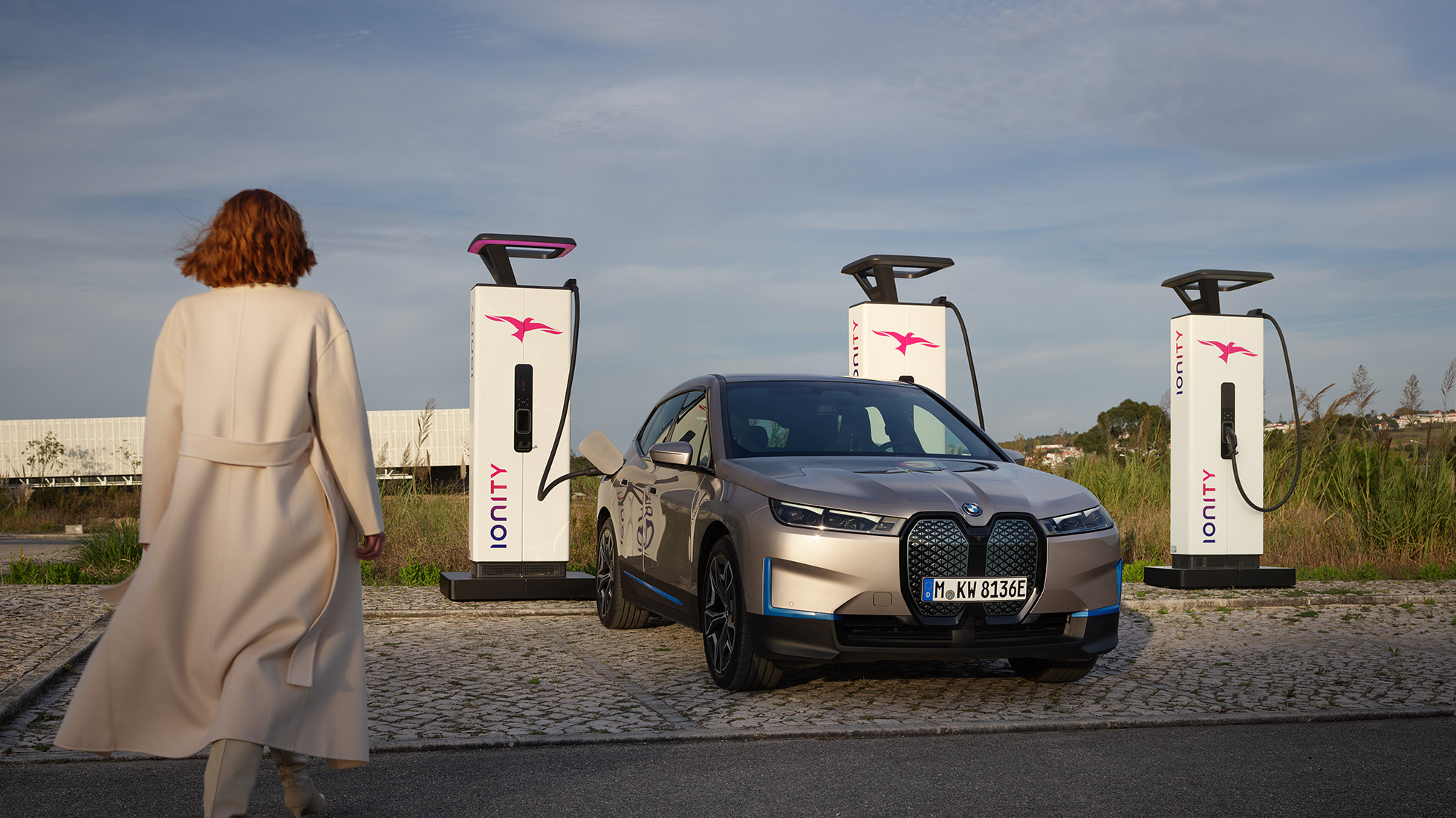 BMW iX μπροστινή λήψη τρία τέταρτα σε σταθμό φόρτισης BMW iX Cashmere Silver i20 μπροστινή λήψη τρία τέταρτα σε σταθμό φόρτισης