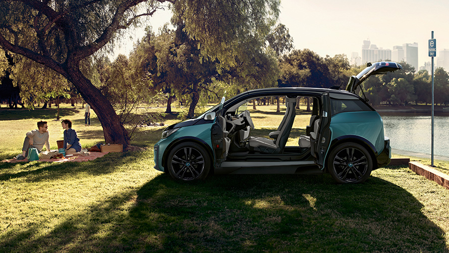 BMW i3 2018, σε πάρκο BMW i3 I01 2018, μπεζ Jucaro με διακοσμητικά στοιχεία σε γκρι Frozen μεταλλικό, πλαϊνή λήψη με ανοικτές πόρτες σε πάρκο