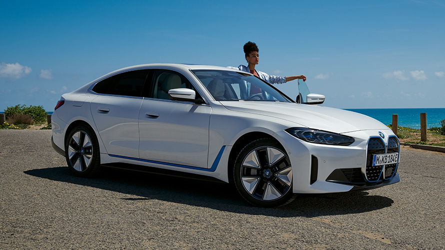 Δύο άτομα στέκονται δίπλα από την BMW i4 G26, μπροστινή λήψη τριών τετάρτων Δύο άτομα στέκονται δίπλα από την BMW i4 G26, μπροστινή λήψη τριών τετάρτων