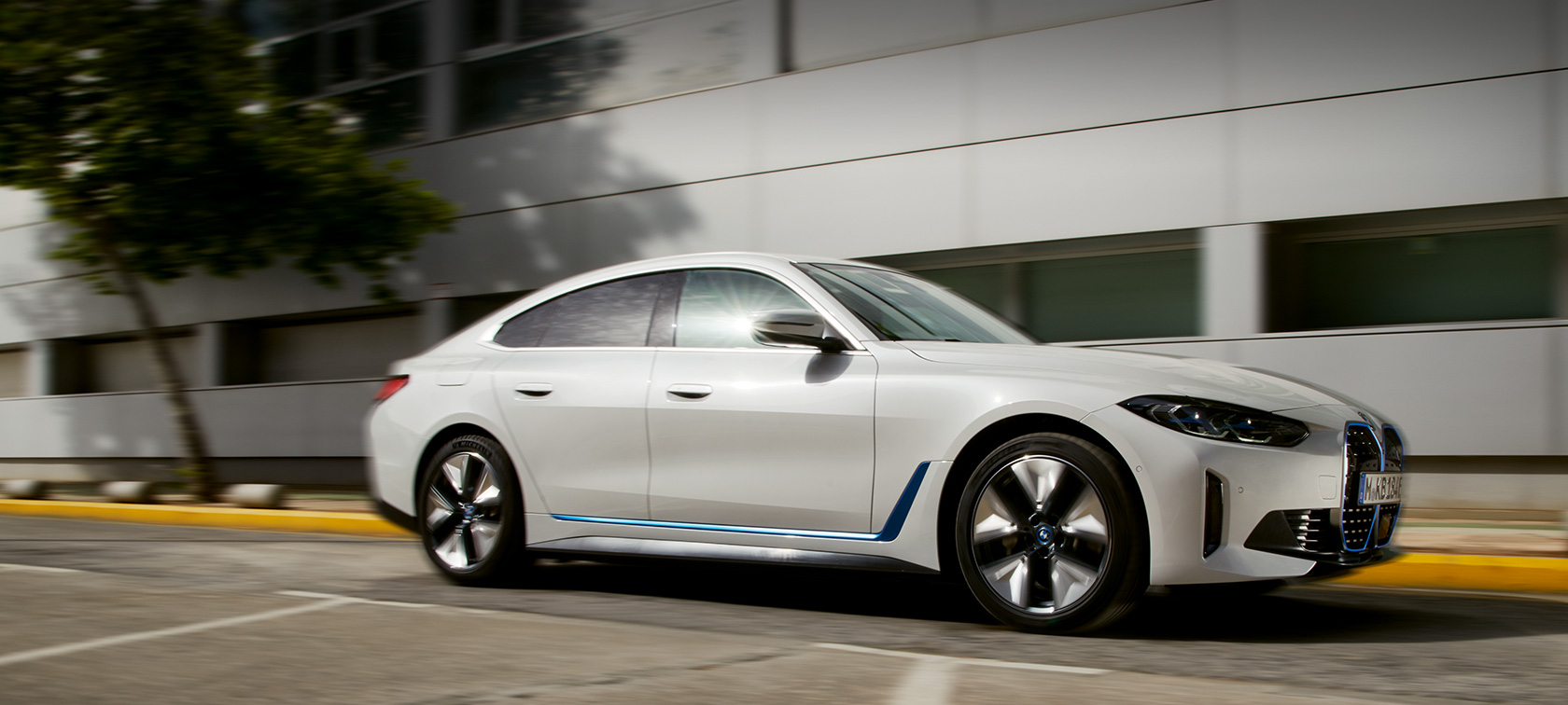 BMW i4 eDrive40, G26, 2021, πλαϊνή λήψη τριών τετάρτων, κινούμενη μπροστά από κτίριο BMW i4 eDrive40, G26, 2021, πλαϊνή λήψη τριών τετάρτων, κινούμενη μπροστά από κτίριο