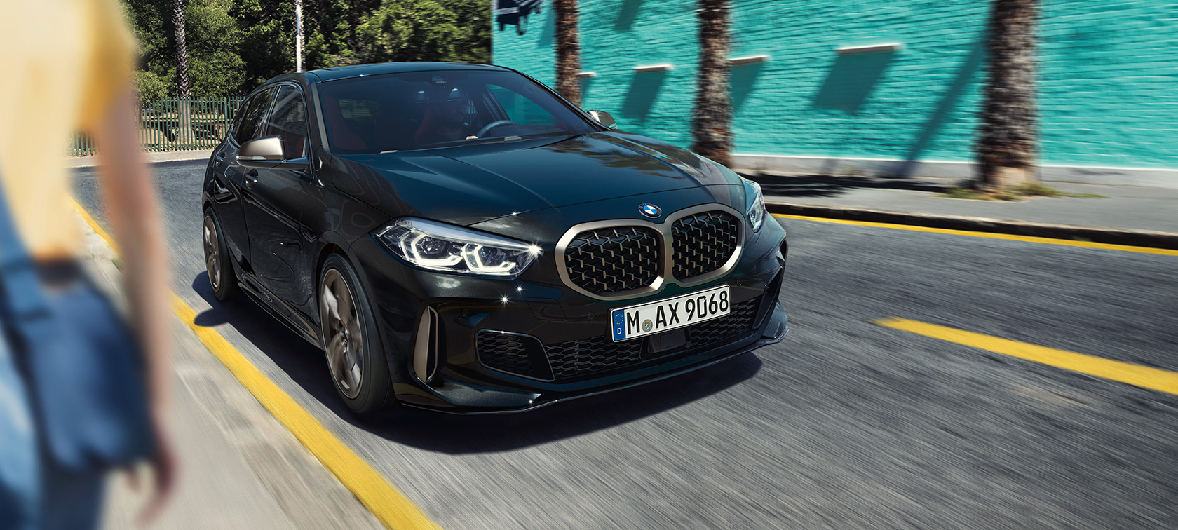 BMW M135i xDrive, μπροστινή λήψη τριών τετάρτων. BMW M135i xDrive σε μαύρο Sapphire μεταλλικό, μπροστινή λήψη τριών τετάρτων, σε κίνηση.