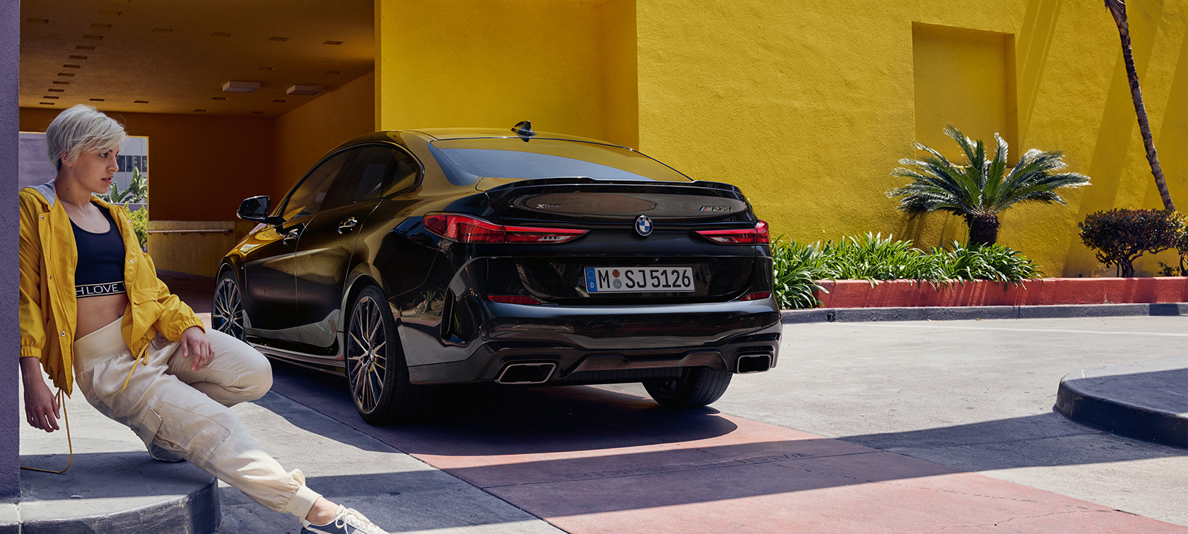 BMW M235i xDrive Gran Coupé , πίσω λήψη τριών τετάρτων BMW M235i xDrive Gran Coupé, μαύρο Black μεταλλικό, F44, πίσω λήψη τριών τετάρτων με γυναίκα στο μπροστινό μέρος