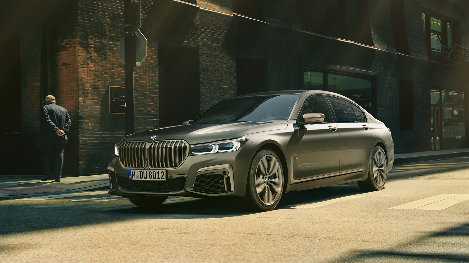 BMW M760Li xDrive Sedan σε αστικό σκηνικό BMW M760Li xDrive Sedan, πλαϊνή μπροστινή λήψη, κινούμενη σε δρόμο μπροστά σε αστικό σκηνικό