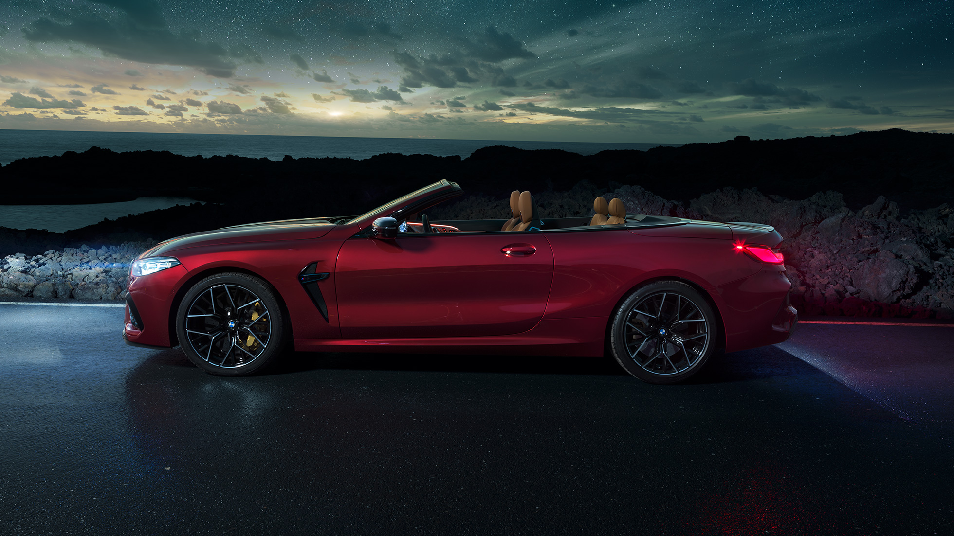 BMW M8 Competition Cabrio, πλαϊνή λήψη. BMW Μ8 Competition Cabrio σε κόκκινο Motegi μεταλλικό με ανοικτή υφασμάτινη οροφή, πλαϊνή λήψη, σταθμευμένη, νύχτα κάτω από έναστρο ουρανό.