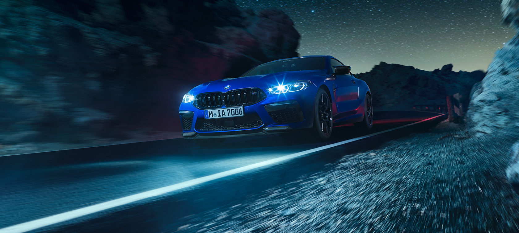 BMW Μ8 Competition Coupé, μπροστινή λήψη τριών τετάρτων. BMW M8 Competition Coupé σε μπλε Marina Bay μεταλλικό, μπροστινή λήψη τριών τετάρτων, κινούμενη τη νύχτα.