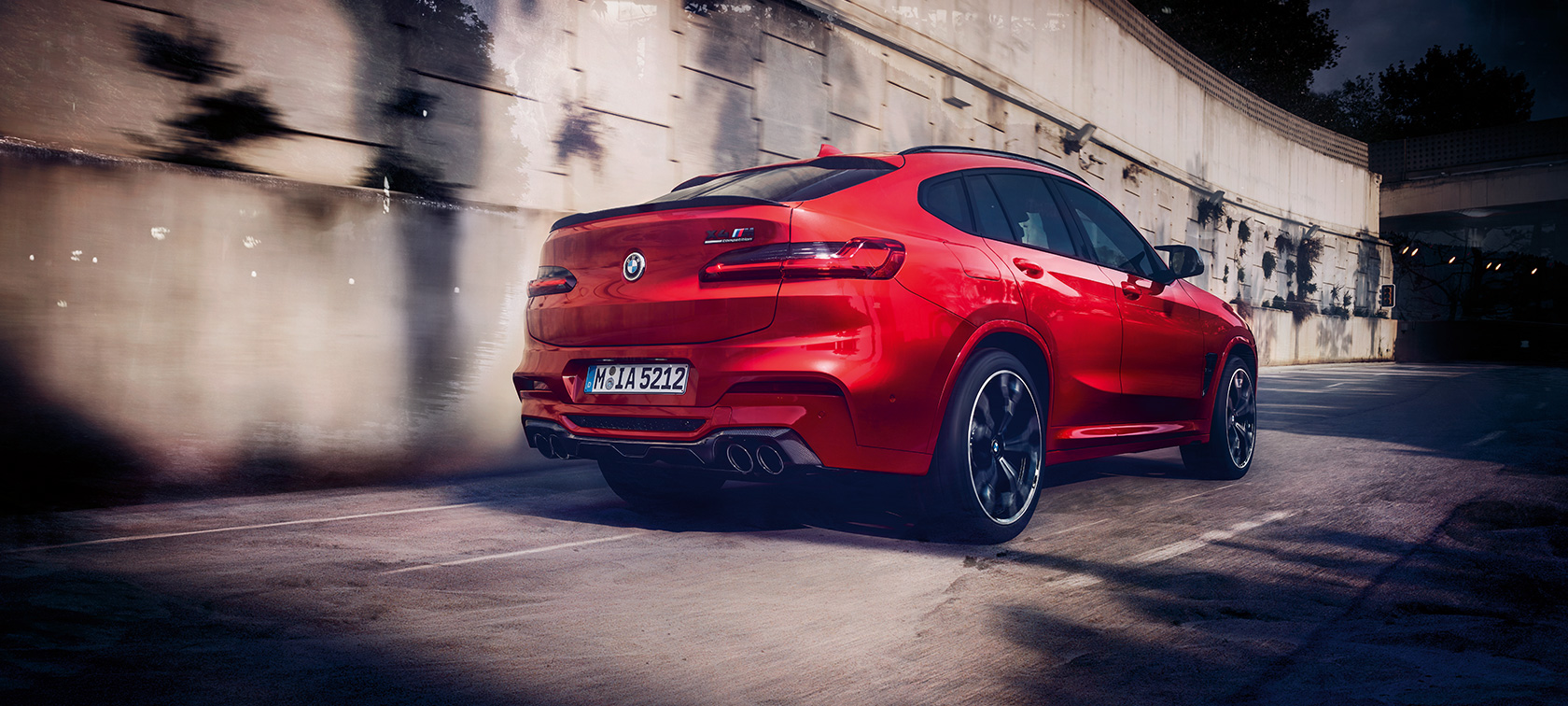 BMW X4 Μ Competition, πίσω λήψη τριών τετάρτων. BMW X4 M Competition σε κόκκινο Toronto μεταλλικό, σε κίνηση, εξωτερικό, πίσω λήψη τριών τετάρτων.