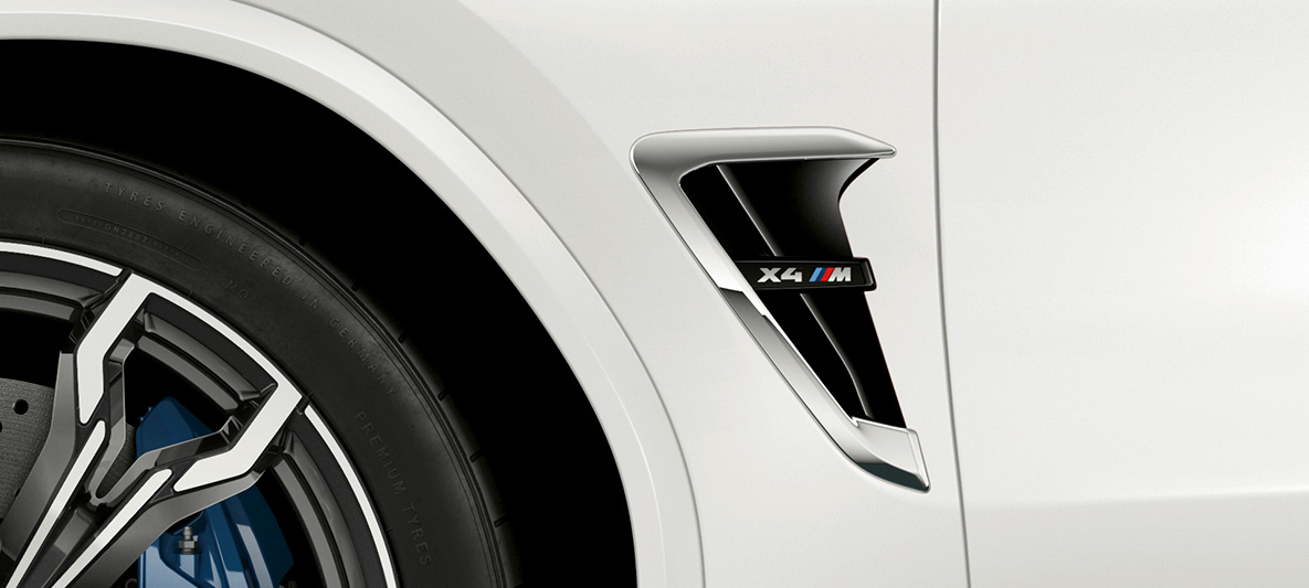 BMW X4 M, πλευρικές εισαγωγές αέρα Μ. BMW X4 M σε λευκό Alpine, εξωτερικό, πλευρικές εισαγωγές αέρα με χρωμιωμένες λεπτομέρειες και επιγραφή μοντέλου.