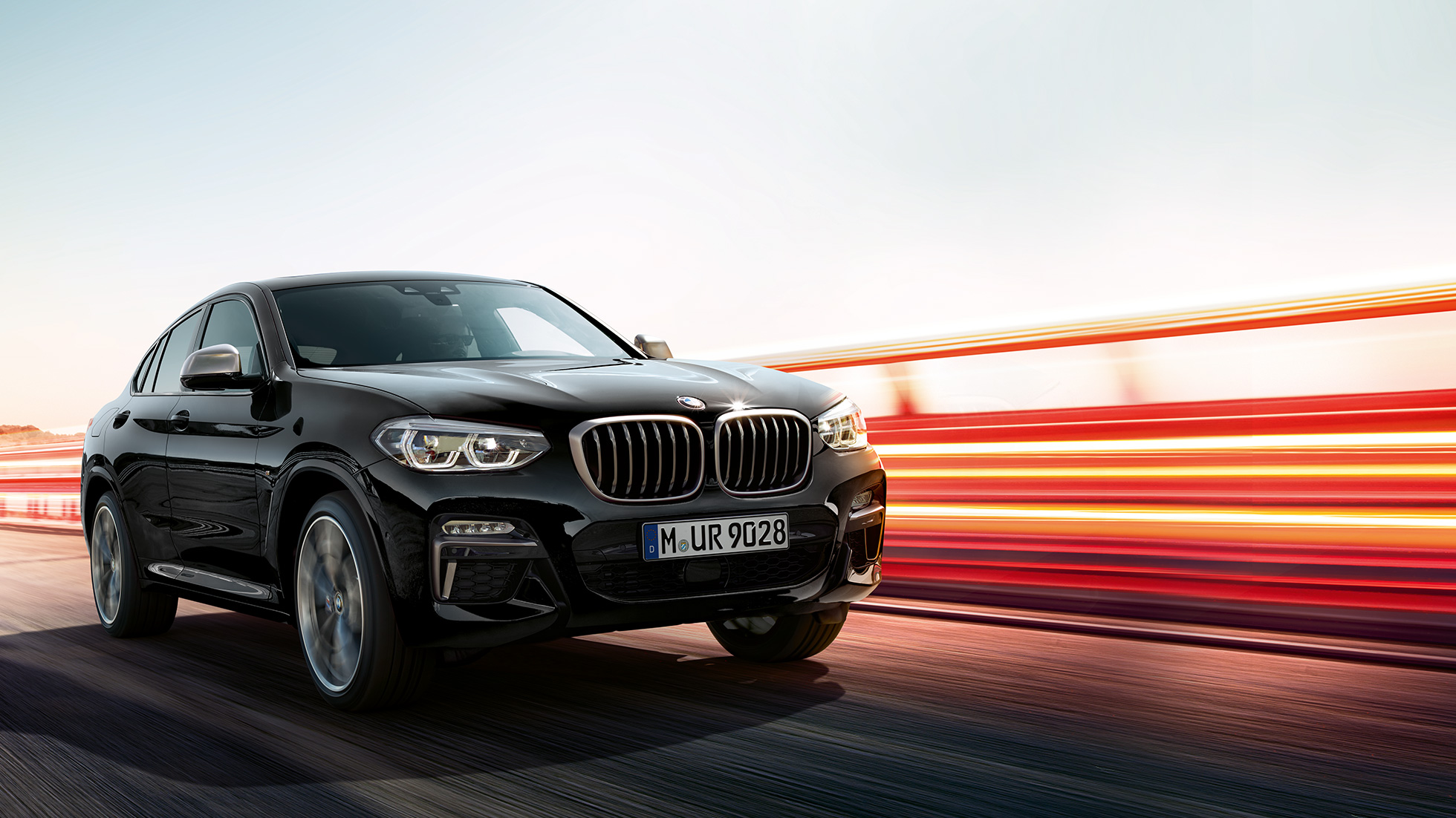 BMW X4 M40i, πίσω λήψη τριών τετάρτων. BMW X4 M40i σε μαύρο Sapphire μεταλλικό, σε κίνηση, εξωτερικό, πίσω λήψη τριών τετάρτων με φωτεινές γραμμές.