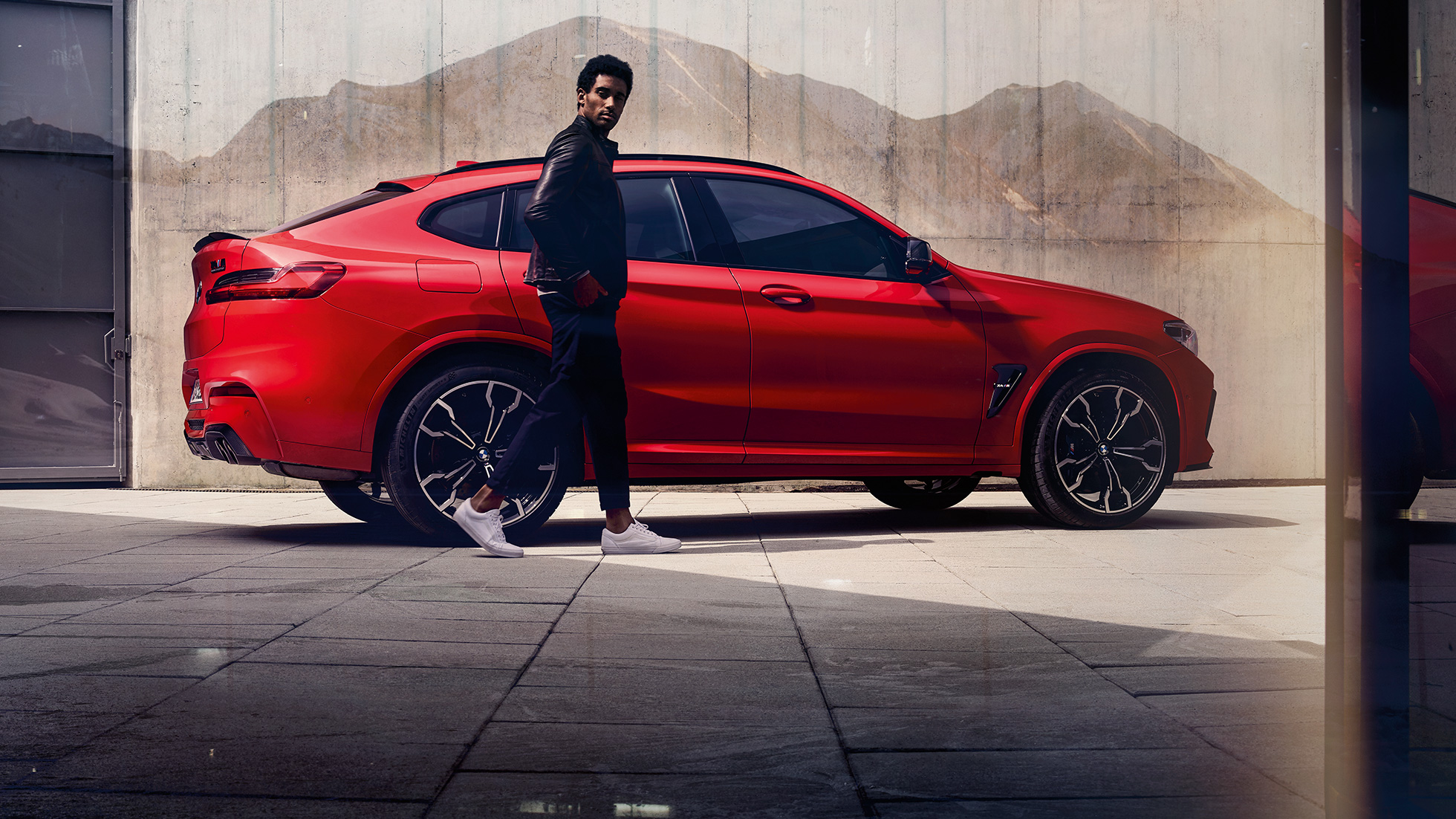 BMW X4 M Competition, πλαϊνή λήψη με νεαρό άντρα. BMW X4 M Competition σε κόκκινο Toronto μεταλλικό, εξωτερικό, πλαϊνή λήψη με νεαρό άντρα.