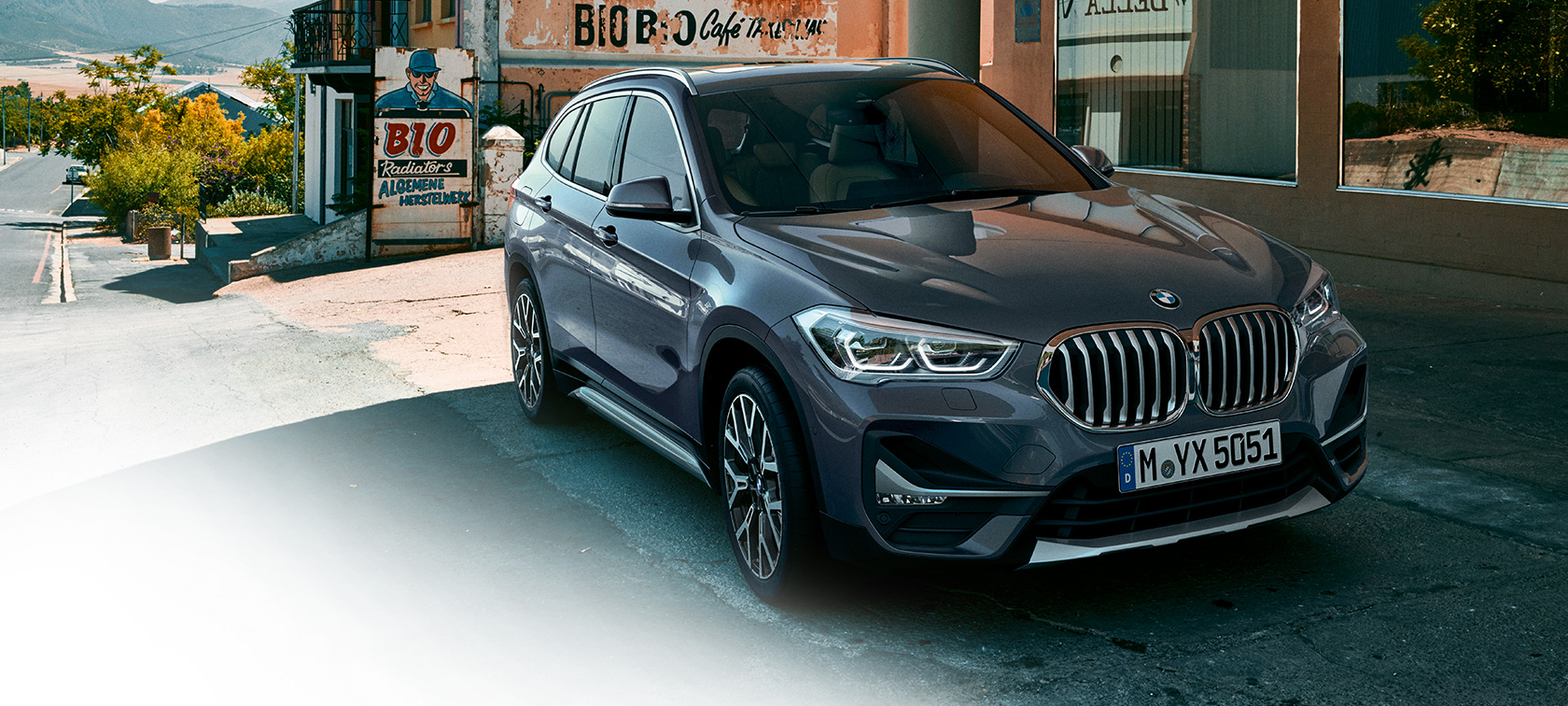 BMW X1, μπροστινή λήψη τριών τετάρτων. BMW X1, μπροστινή λήψη τριών τετάρτων, σταθμευμένη μπροστά από αστικό σκηνικό.