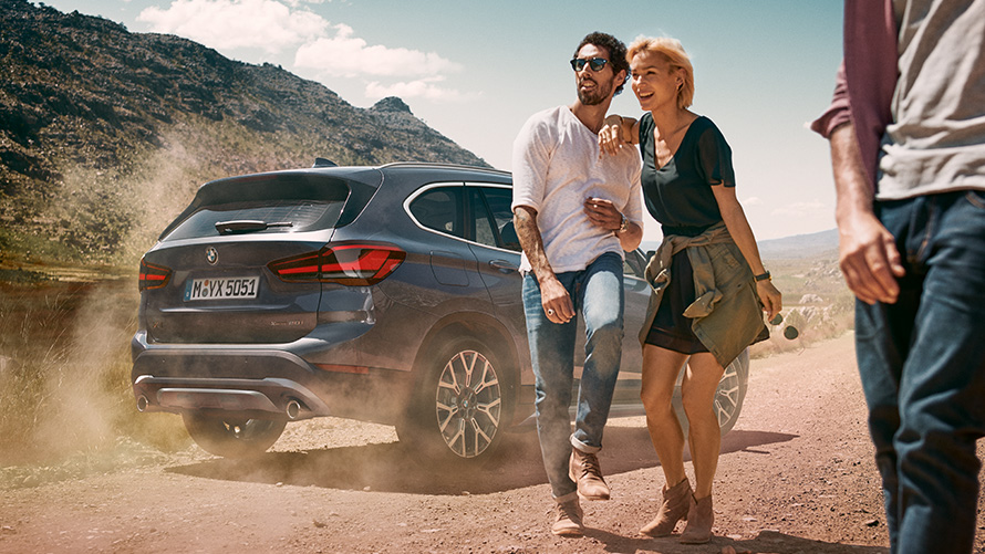 BMW X1, F48, LCI, Storm Bay, πίσω λήψη τριών τετάρτων BMW X1, F48, LCI, Storm Bay, πίσω λήψη τριών τετάρτων, σταθμευμένη, με ανθρώπους μπροστά σε τοπίο