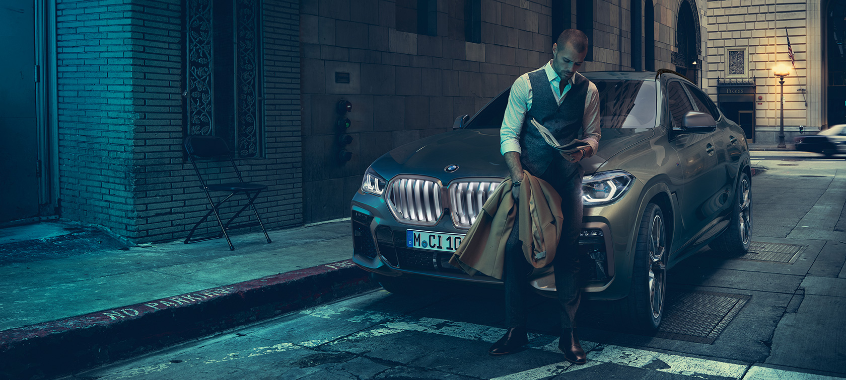 Άντρας στηρίζεται στην BMW X6. Άντρας στηρίζεται στην BMW X6, πλαϊνή λήψη μπροστά από αστικό σκηνικό.