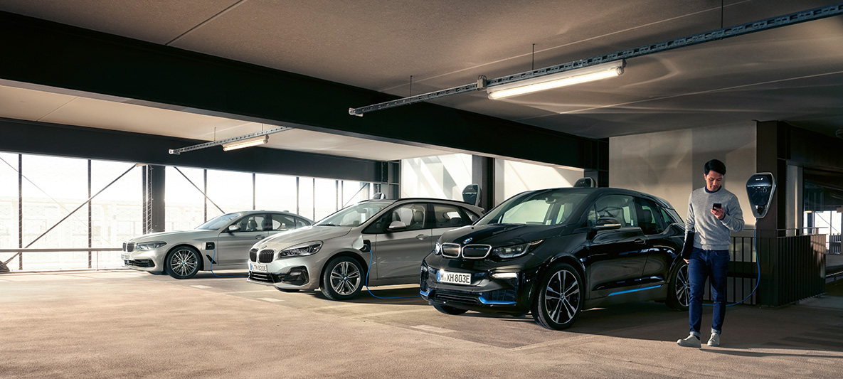 Ηλεκτρικά αυτοκίνητα BMW και υβριδικά μπροστά σε σταθμό φόρτισης BMW tax incentives BMW electric cars and hybrid vehicles man at charging station