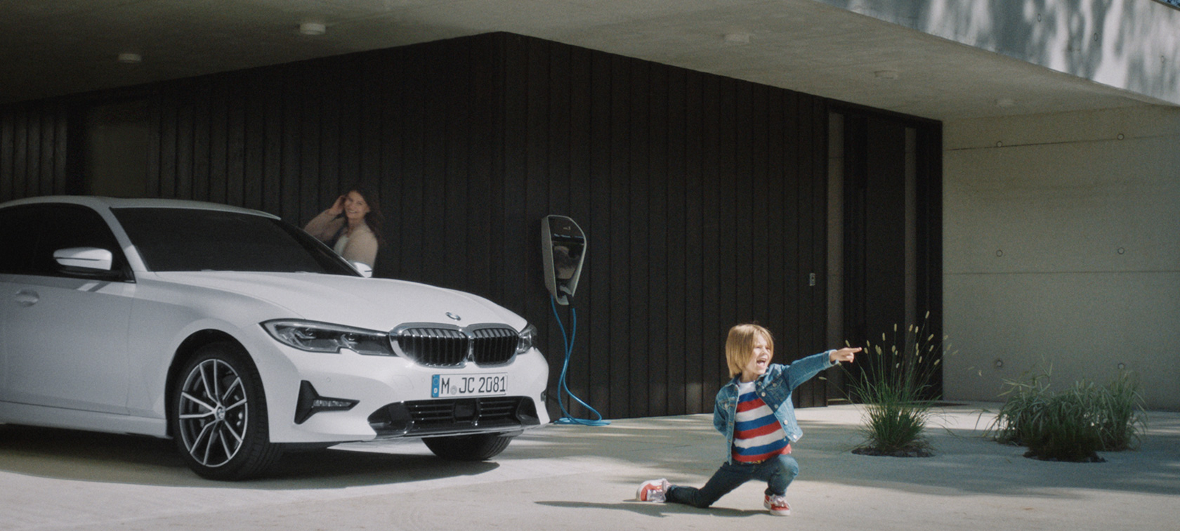Υβριδικό BMW σε σταθμό φόρτισης BMW Plug-in Hybrid, αγόρι μπροστά από υβριδικό BMW σε σταθμό φόρτισης
