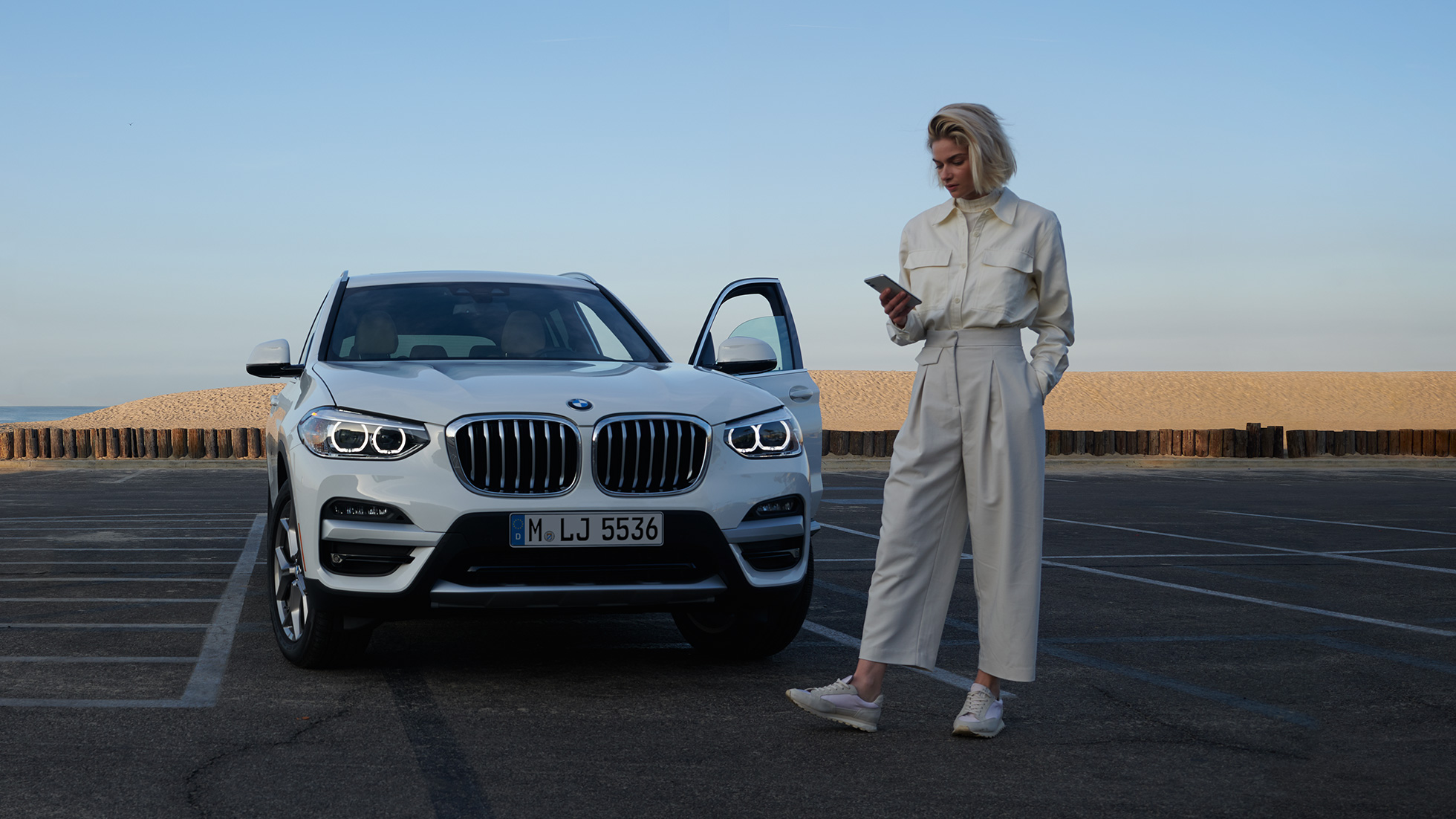 Γυναίκα χρησιμοποιεί την εφαρμογή My BMW στο smartphone Γυναίκα χρησιμοποιεί την εφαρμογή My BMW του BMW ConnectedDrive στο smartphone, μπροστά από μία λευκή BMW X5