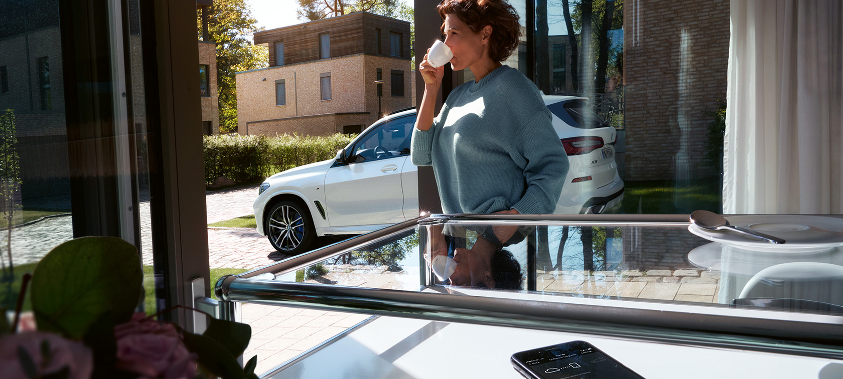 BMW Απομακρυσμένη Αναβάθμιση Λογισμικού Γυναίκα πίνει από ένα φλιτζάνι καθώς η BMW Απομακρυσμένη Αναβάθμιση Λογισμικού αναβαθμίζει το λογισμικό της BMW X5