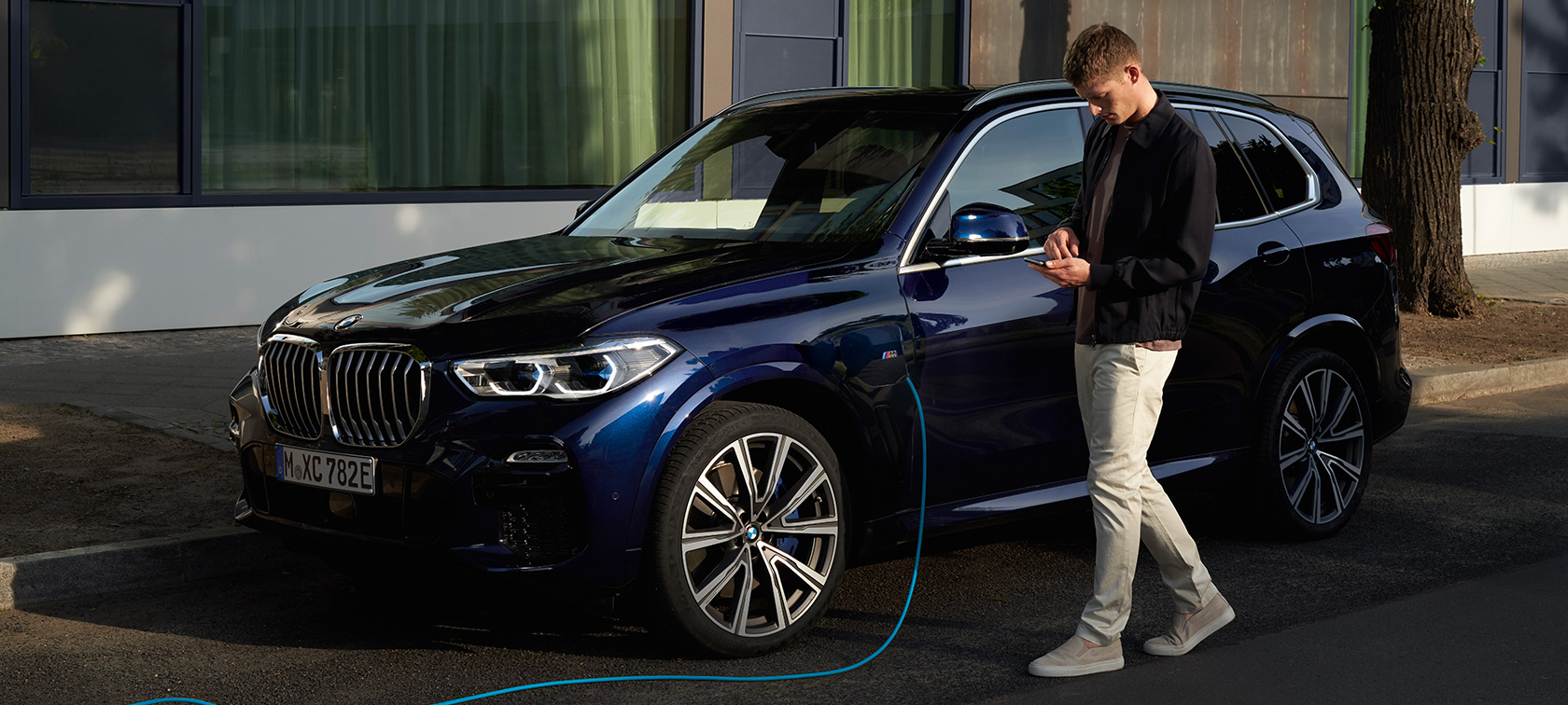 Άντρας χρησιμοποιεί την εφαρμογή My BMW στο smartphone Άντρας χρησιμοποιεί την εφαρμογή My BMW του BMW ConnectedDrive στο smartphone, καθώς φορτίζει την plug-in υβριδική BMW X5