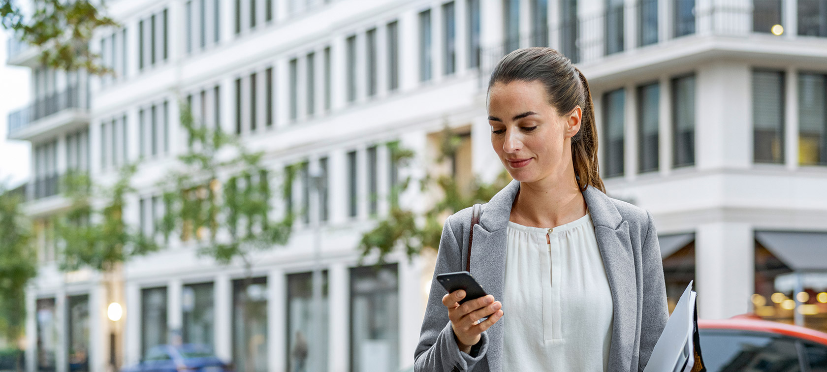 Γυναίκα μπροστά από κτίριο κοιτά το smartphone Απομακρυσμένη Αναβάθμιση Λογισμικού, γυναίκα μπροστά από κτίριο κοιτά το smartphone