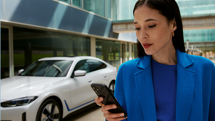 Γυναίκα στέκεται μπροστά από μία BMW Γυναίκα στέκεται μπροστά από μία BMW και κοιτάζει στο smartphone