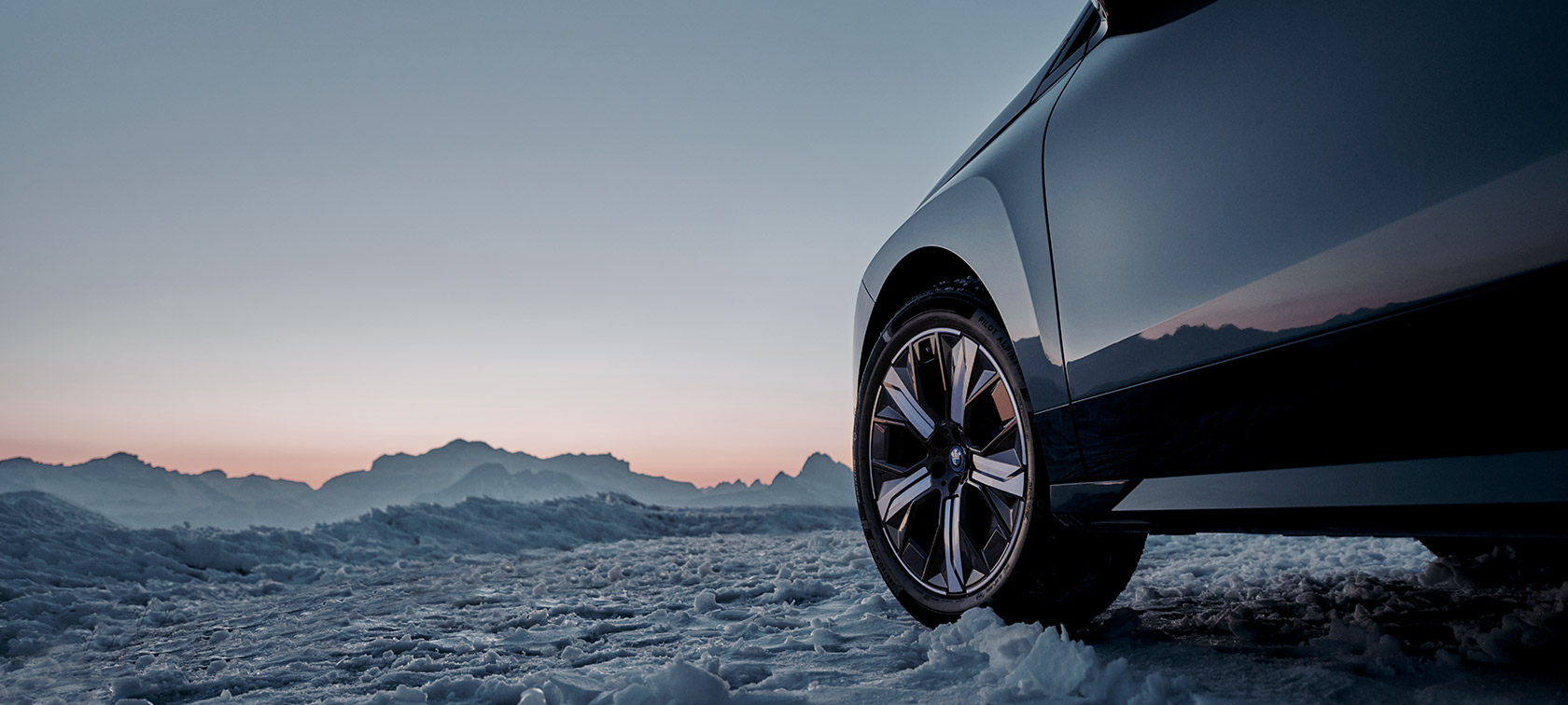 Γνήσιοι Τροχοί BMW για την BMW iX (I20) στο χιόνι μπροστά από τα βουνά. Γνήσιοι Τροχοί BMW για την BMW iX (I20) στο χιόνι μπροστά από τα βουνά.