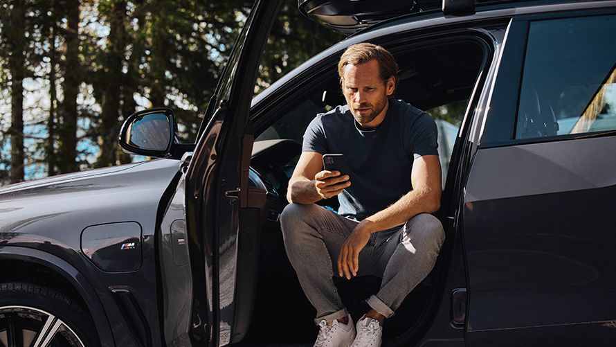 Άντρας κάθεται σε μία BMW και κοιτά το smartphone BMW Αξεσουάρ για την Άνοιξη και το Καλοκαίρι, άντρας κάθεται σε μία BMW και κοιτά το smartphone