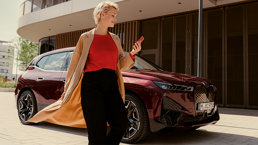 Εφαρμογή My BMW, γυναίκα με smartphone μπροστά από μία BMW Γυναίκα με smartphone μπροστά από μία BMW