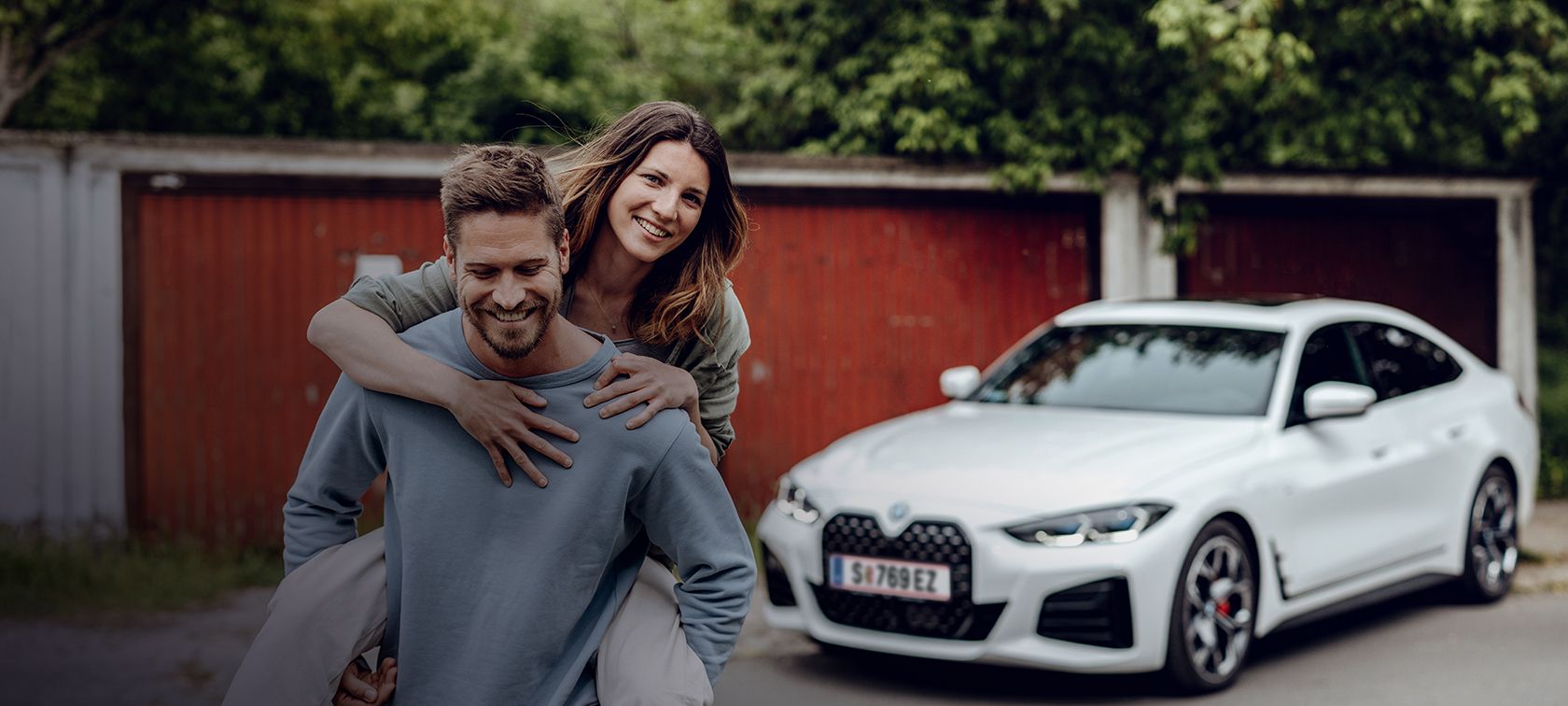 Χαμογελαστός άντρας απομακρύνεται από την BMW i4 κουβαλώντας μία χαμογελαστή γυναίκα στην πλάτη του. Χαμογελαστός άντρας απομακρύνεται από την BMW i4 κουβαλώντας μία χαμογελαστή γυναίκα στην πλάτη του.