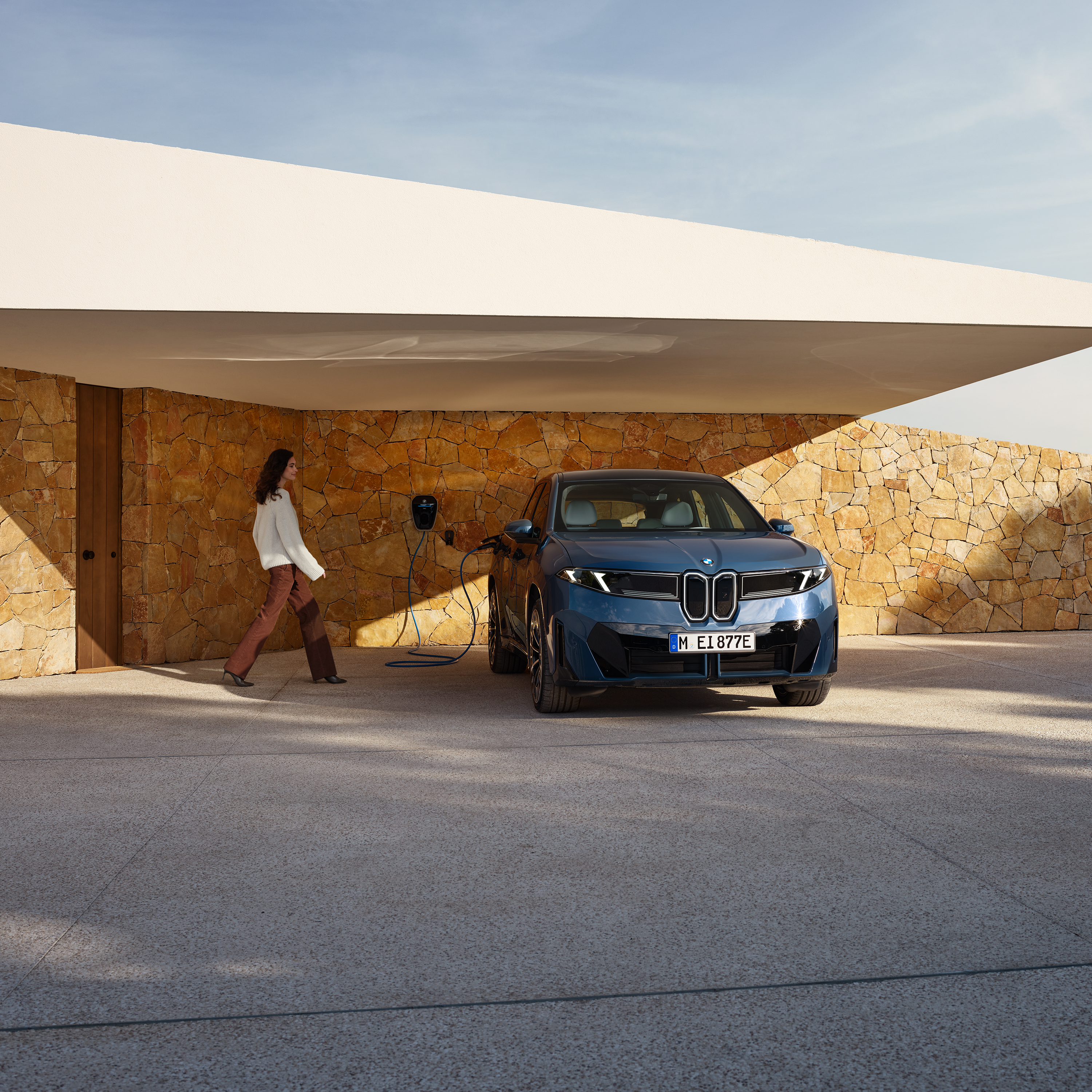Μια γυναίκα περπατά προς μια BMW iX3 συνδεδεμένη σε wallbox