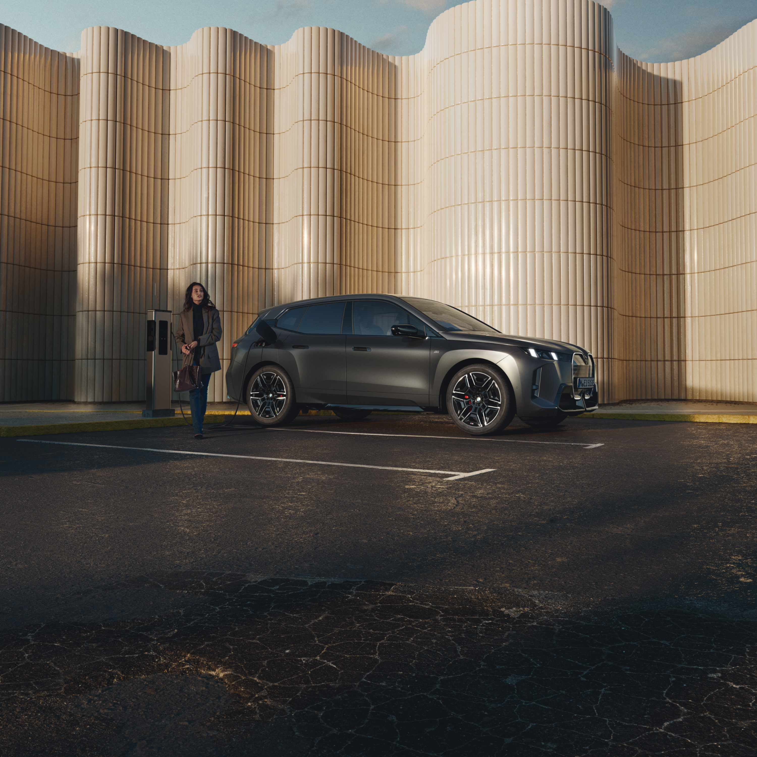 Ένας άνθρωπος στηρίζεται σε μια BMW σε δημόσιο σταθμό φόρτισης στην άκρη του δρόμου